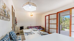 Een eethoek met een tafel voor twee personen, een bank, een televisie en een deur naar buiten.