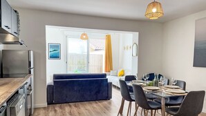 A modern kitchen with a built-in oven and dishwasher, a dining area with a glass table and dark chairs, and a cozy seating area with a blue sofa and yellow cushions. - Cap Océan by Interhome (Capbreton)
