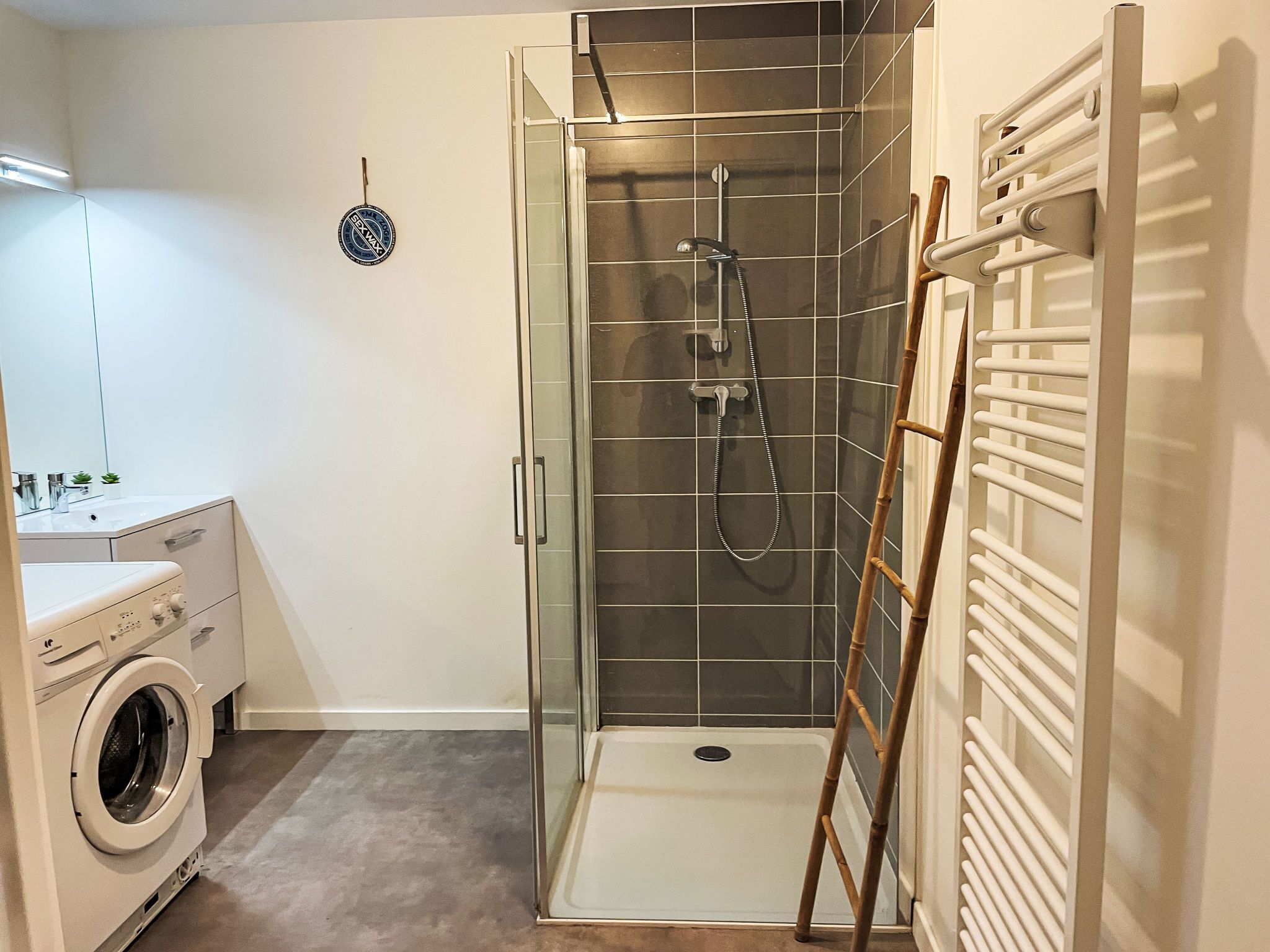 A compact bathroom with a glass-enclosed shower, a built-in washing machine, and a towel rack.