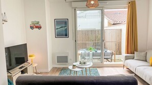 A modern living room with a TV, sofa, and a balcony with a table and chairs. - Cap Océan by Interhome (Capbreton)