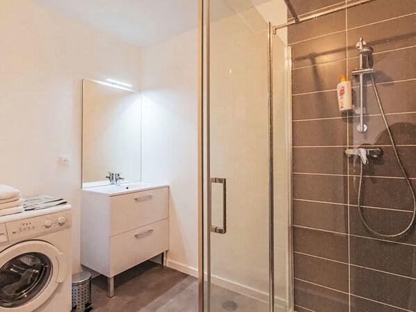 Une salle de bain moderne avec une douche à parois de verre, un lavabo blanc et un lave-linge.