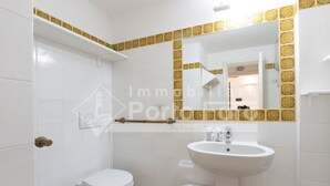 A bathroom with a toilet, bidet, and sink, featuring white tiles and a decorative golden border.