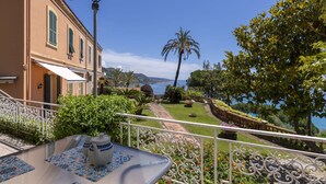 A terrace with a table set for tea, overlooking a scenic coastal view with a building and lush greenery. - Beautiful apartment for 4 guests with WIFI, pool, TV, terrace and panoramic view (Ventimiglia)