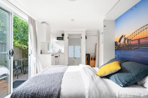 Habitación de hotel moderna con una cama grande, vistas de la Ópera de Sídney y una kitchenette.