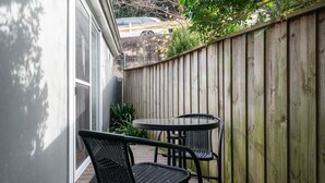 Un patio con due sedie in metallo nero e un piccolo tavolo rotondo, circondato da un recinto in legno e un muro bianco.