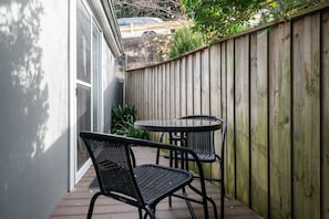 Un patio con dos sillas de metal negro y una pequeña mesa redonda, rodeado por una valla de madera y una pared blanca.
