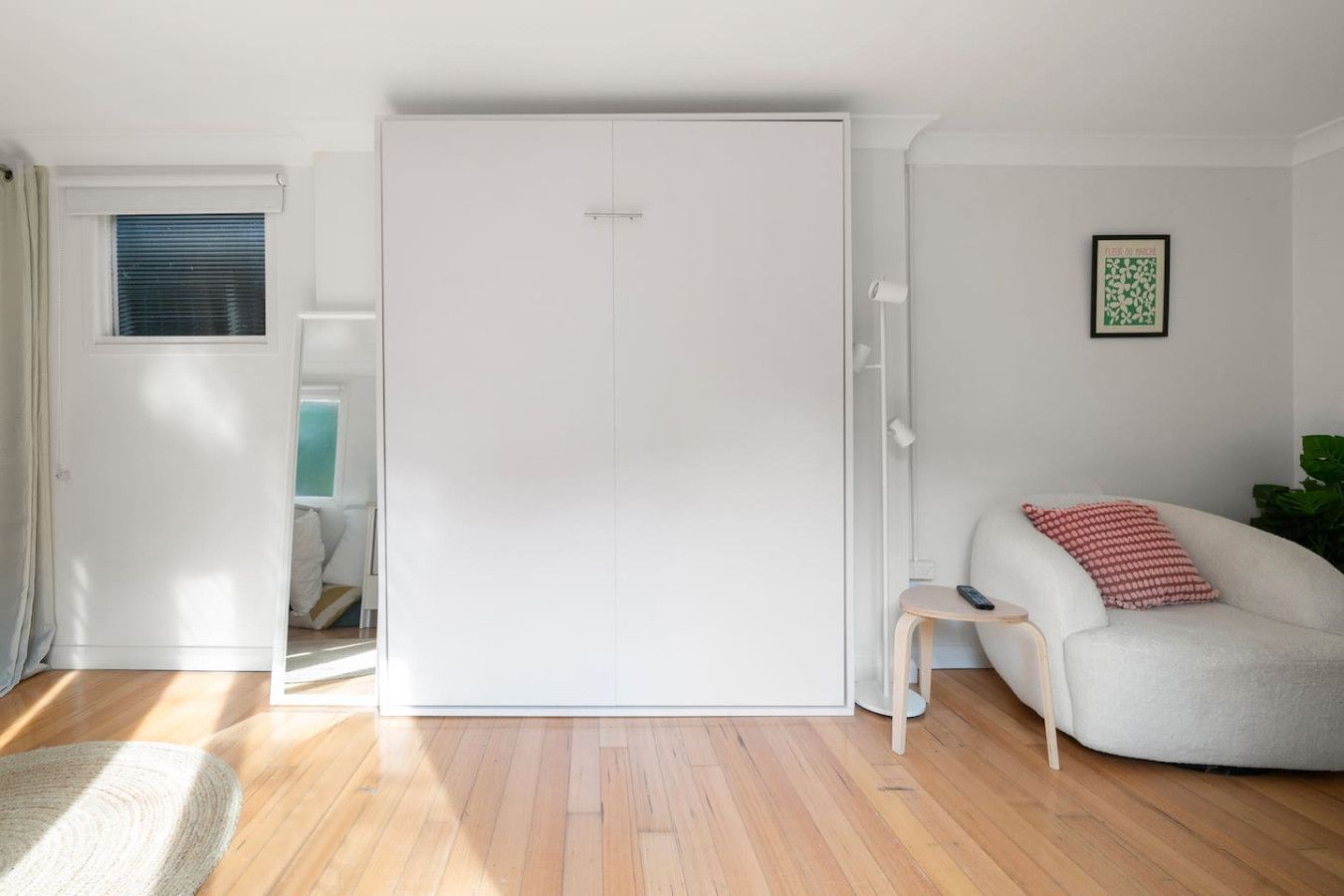 A modern room with a sliding wardrobe, a sofa with a red pillow, and a framed picture on the wall.