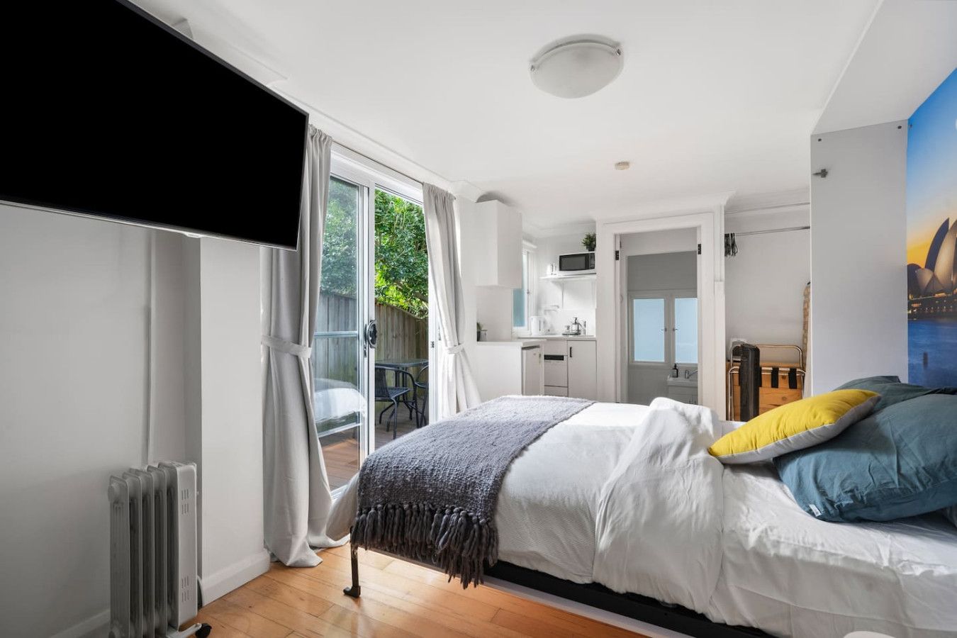 A modern bedroom with a bed, a view of the outdoors, a kitchenette, and a bathroom.