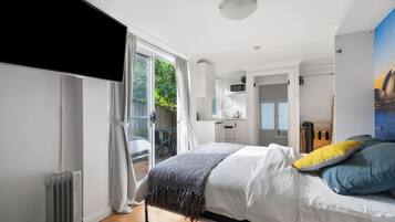 A modern bedroom with a bed, a view of the outdoors, a kitchenette, and a bathroom.