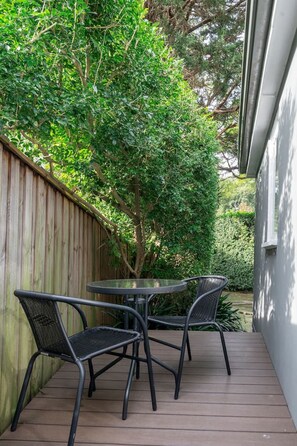 Un patio con terraza de madera, una mesa redonda y cuatro sillas.