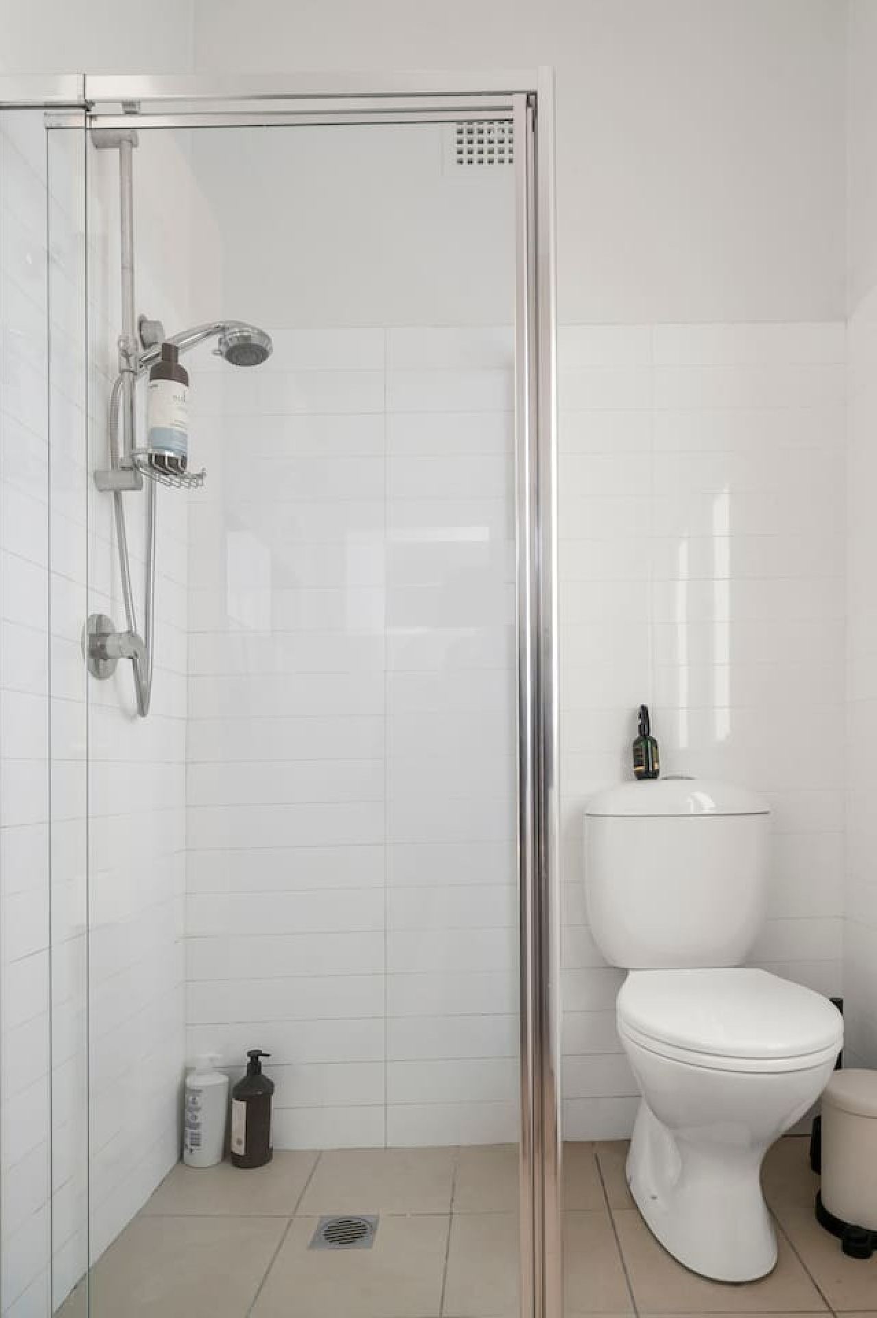 Une salle de bain moderne avec une douche à parois de verre, des toilettes blanches et une petite poubelle.