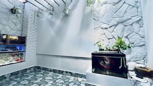 A room with a stone-patterned floor, white walls, and hanging plants. - AULE HOSTEL (Ho Chi Minh City)