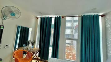 Una habitación de hotel con cama, un escritorio con silla, un ventilador y una ventana con cortinas.