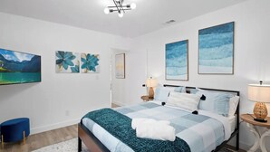 A modern bedroom with a large bed, a flat-screen TV, and artwork on the walls.