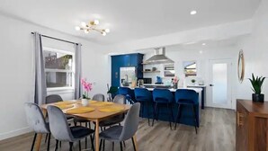A modern kitchen with blue cabinets, a central island, and a dining area with a wooden table and grey chairs.