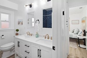Une salle de bain moderne avec un lavabo blanc, deux robinets, un miroir et une zone de douche carrelée de carreaux bleus.