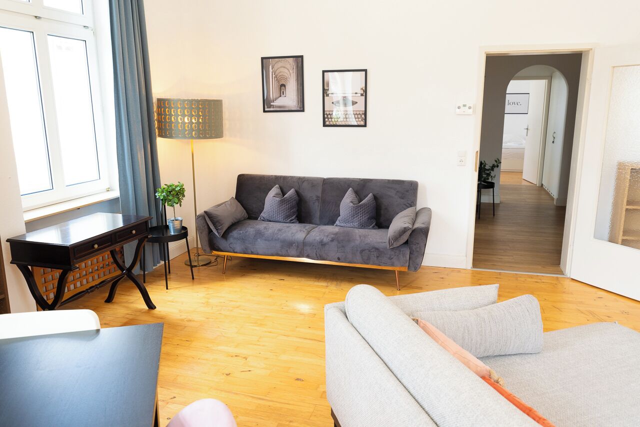 Una sala de estar con un sofá gris, una mesita auxiliar, una lámpara y un cuadro en la pared.