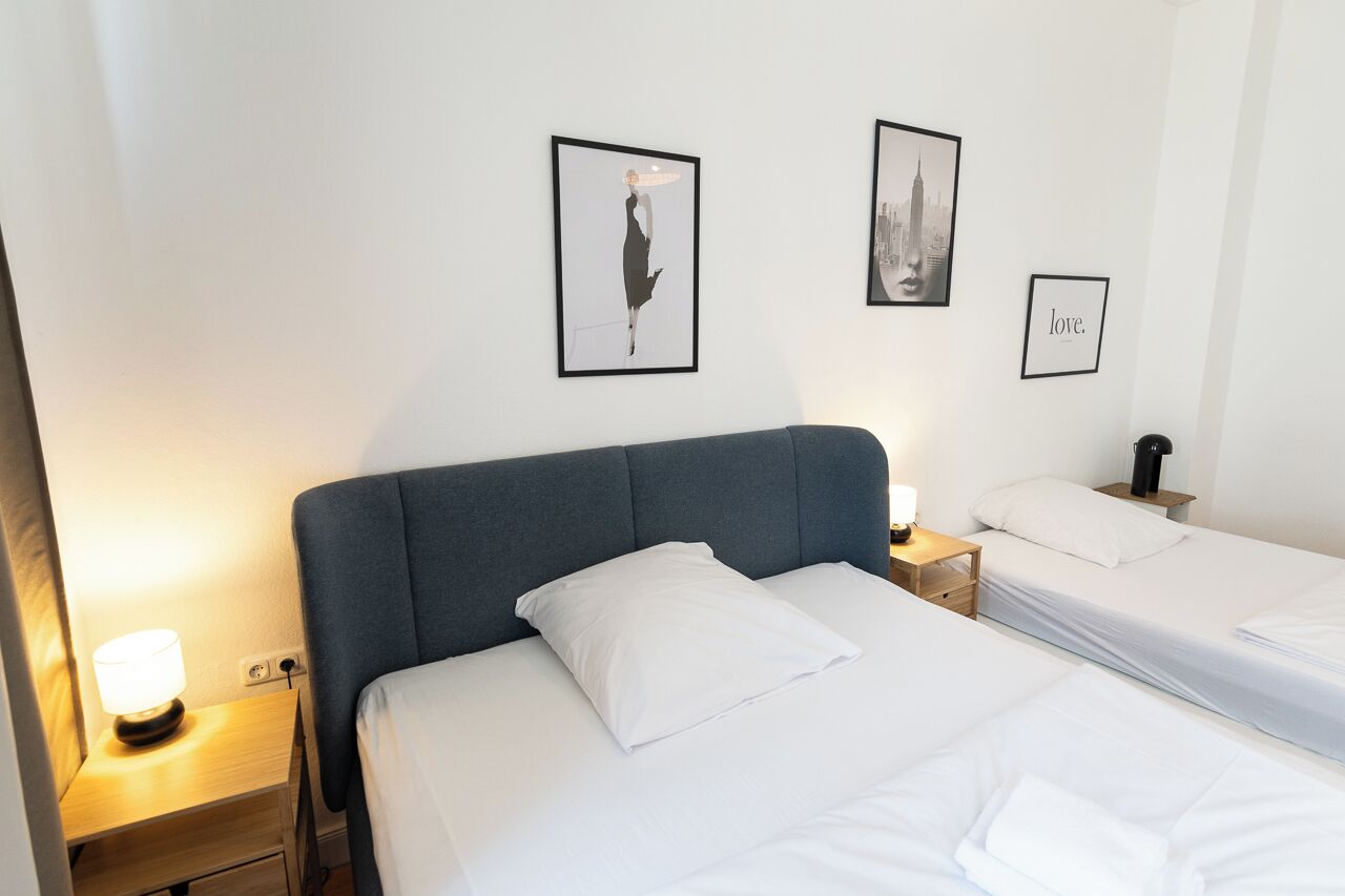 A hotel room with two beds, a nightstand with a lamp, and framed artwork on the wall.