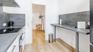 A modern kitchen with grey countertops, a black induction cooktop, stainless steel appliances, and a wooden floor.