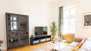 A living room with a sofa, a glass coffee table, a dark cabinet, and a television.