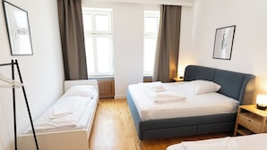 A bedroom with two beds, a wooden floor, and a window with curtains.