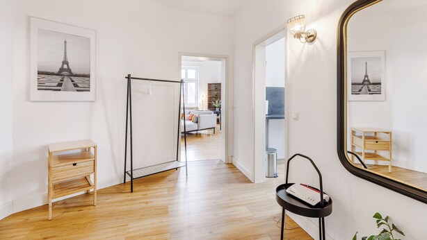 A hotel room with a wooden floor, a large mirror, a small wooden side table, and a framed picture of the Eiffel Tower.