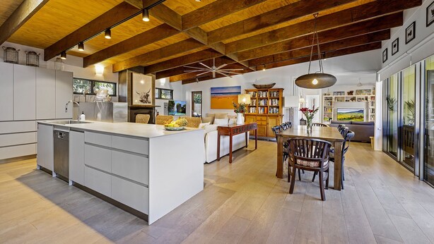 Una cocina amplia con una isla central, vigas de madera en el techo y un comedor con mesa y sillas de madera.
