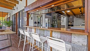Un área de bar con taburetes blancos, una barra de madera y vista a una cocina.