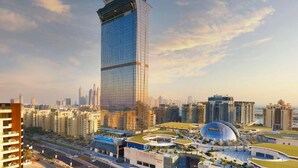 A high-rise building with a modern glass facade, surrounded by other residential and commercial buildings, and a distinctive dome-shaped structure nearby. - Luxurious studio in St Regis Palm View (Dubai)
