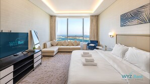 A hotel room with a large bed, a sofa, a TV, and a view of the city. - Luxurious studio in St Regis Palm View (Dubai)