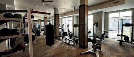 Un gimnasio con diversos equipos de ejercicio, ventanas amplias y suelo de madera.