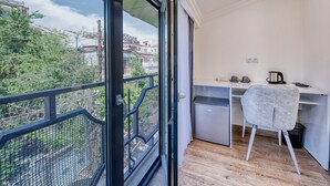 Varanda com vista para edifícios e árvores, uma escrivaninha com cadeira e uma pequena cozinha.