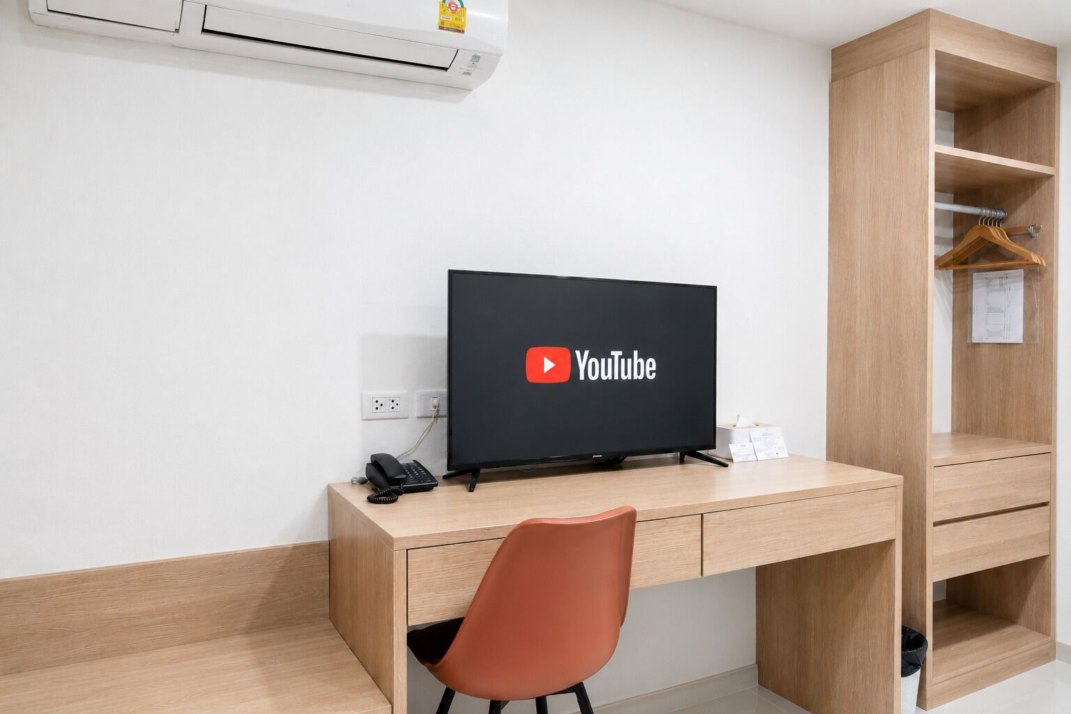 A modern office space with a desk, a computer monitor displaying YouTube, a telephone, and a wooden shelving unit.