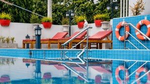 Una piscina con sillas de descanso rojas, un flotador salvavidas y plantas en macetas.
