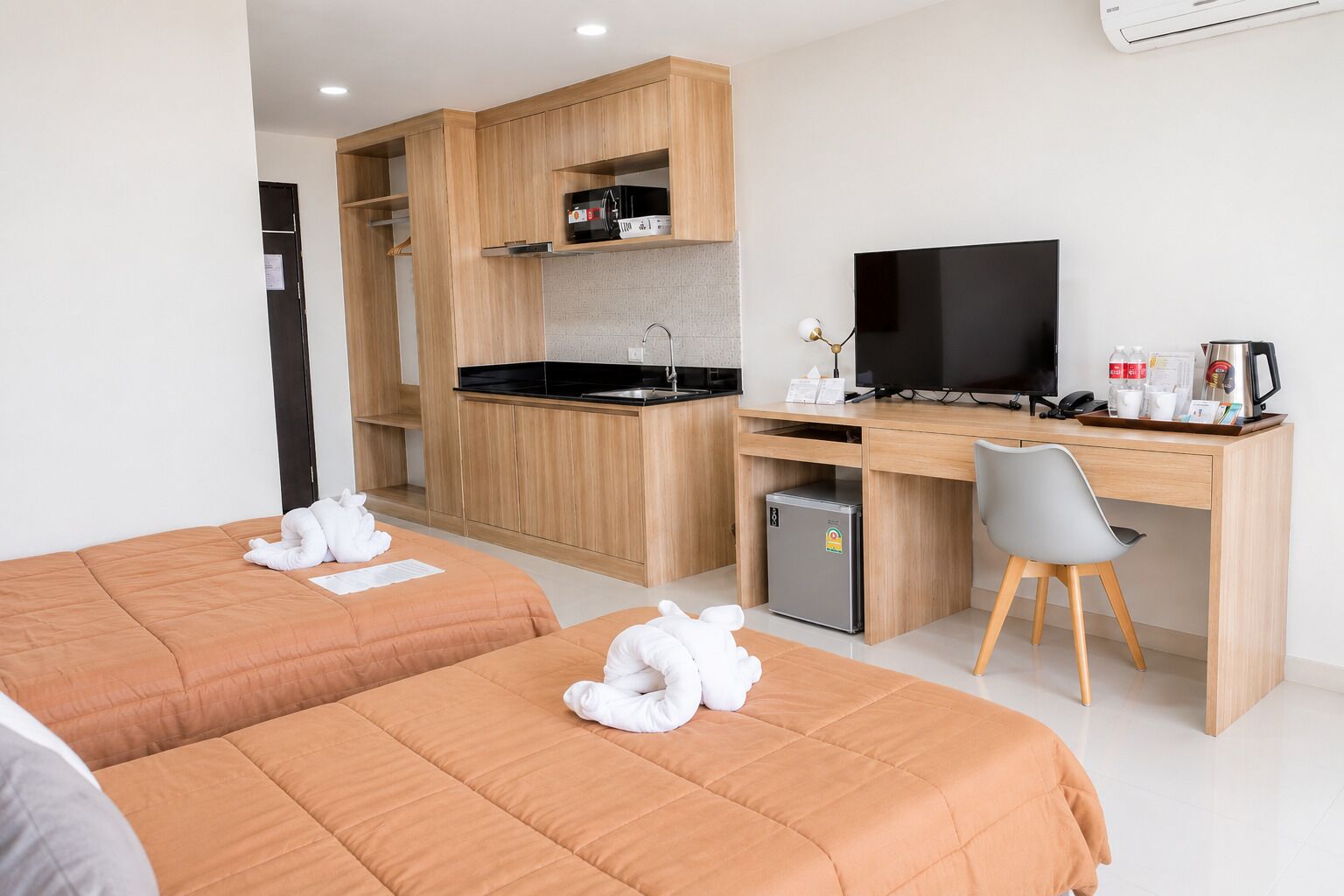 A hotel room with two beds, a kitchenette, a desk with a TV, and a refrigerator.