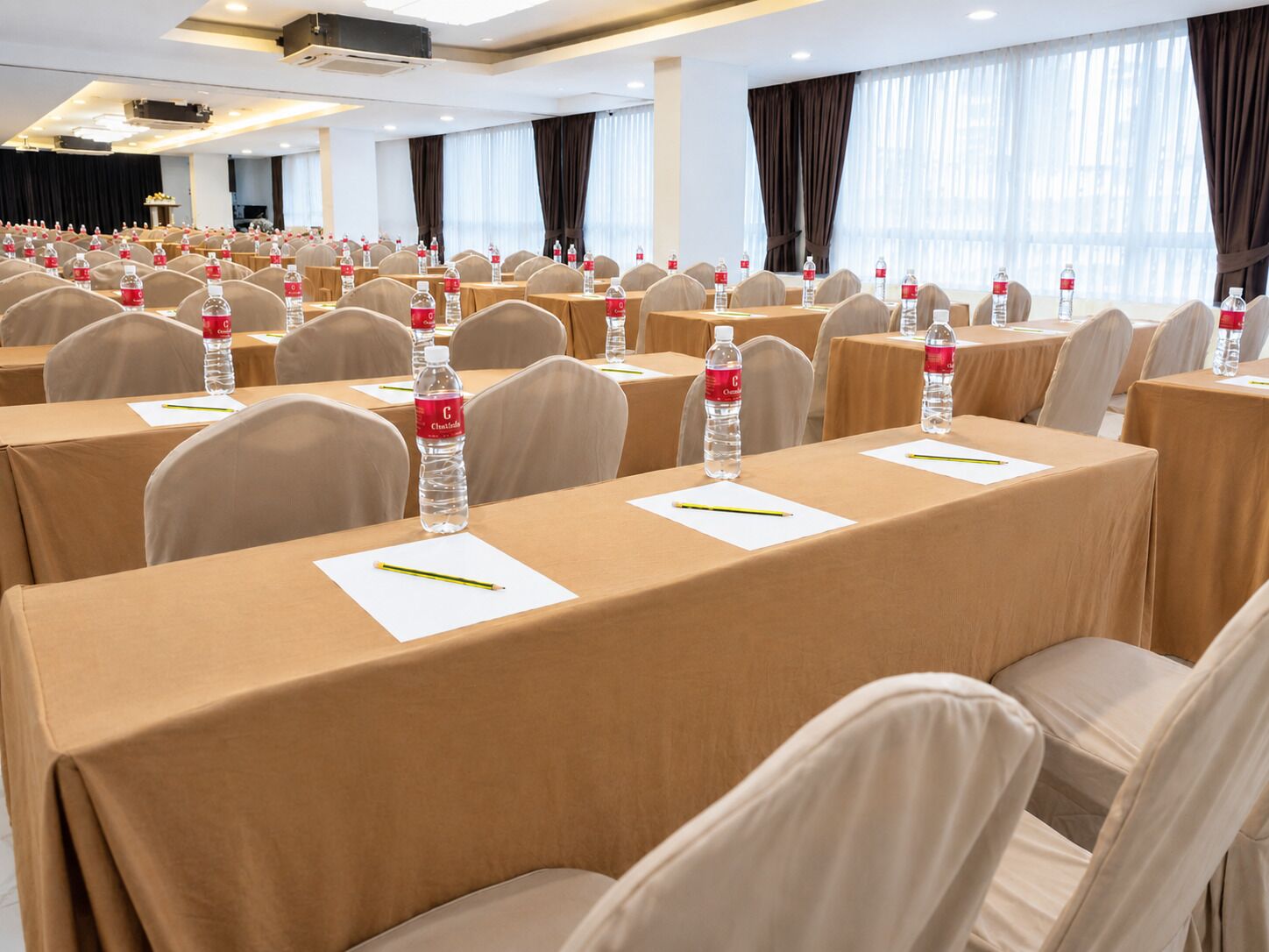 Un salón de conferencias con filas de mesas, sillas y botellas de agua.