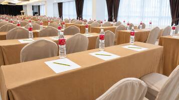 Un salón de conferencias con filas de mesas, sillas y botellas de agua.