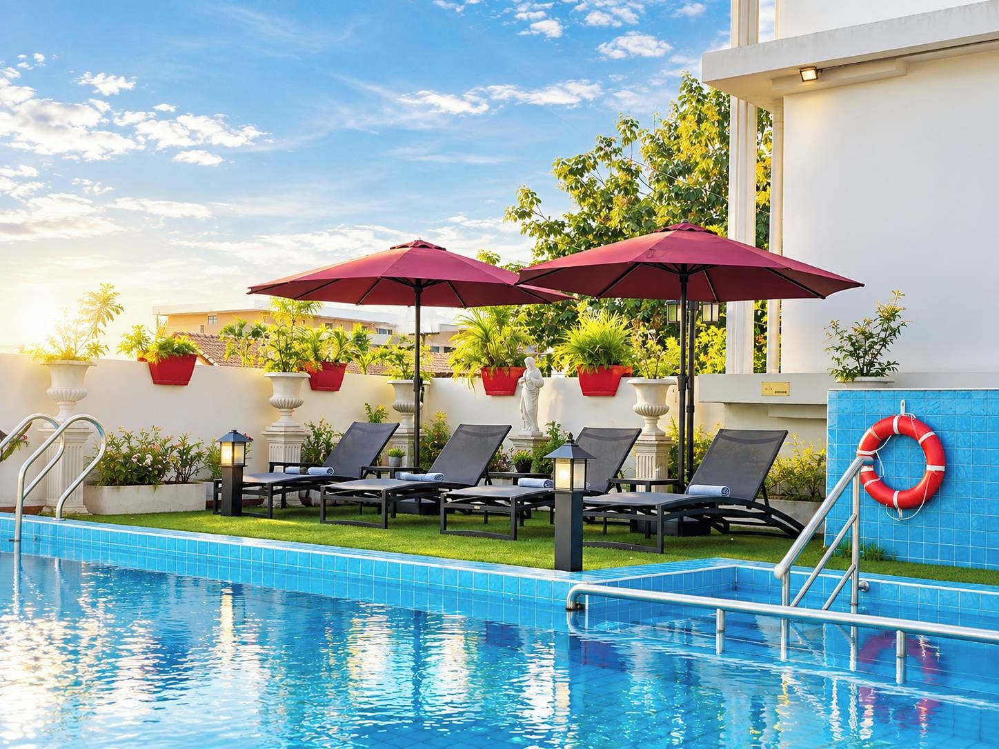 A swimming pool with lounge chairs and umbrellas, surrounded by potted plants and a lifebuoy.