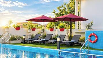 A swimming pool with lounge chairs and umbrellas, surrounded by potted plants and a lifebuoy.