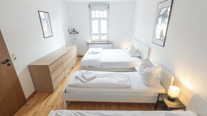 Un dormitorio pequeño y luminoso con dos camas, un aparador de madera, un radiador y una ventana.