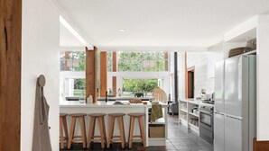 Eine moderne Küche mit Kochinsel, Barhocker, Kühlschrank und Blick auf Grünflächen.