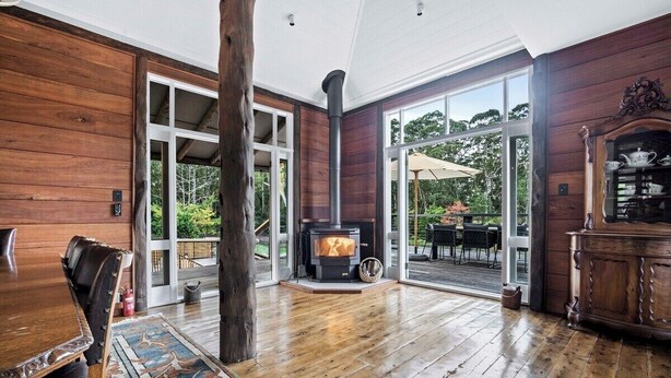 Interior de madera con chimenea, comedor y vistas a un patio exterior a través de puertas de vidrio.
