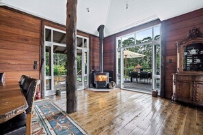 A wooden interior with a fireplace, a dining area, and a view through glass doors to an outdoor patio. - 'Aminya' - Kangaroo Valley Homestead (Kangaroo Valley)