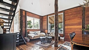Una habitación amplia con paredes de madera, un ventanal grande, una mesa de comedor y una escalera.