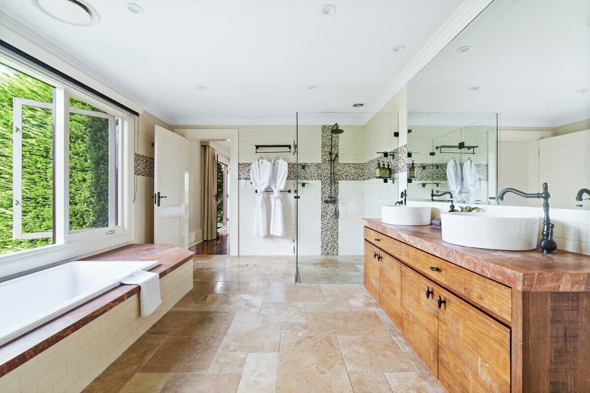 Une salle de bain moderne dotée d’une grande fenêtre, de deux lavabos, d’une douche et d’un meuble-lavabo en bois.