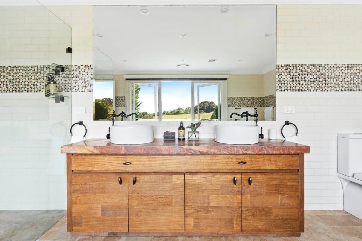 Baño con tocador doble, muebles de madera y un espejo grande.