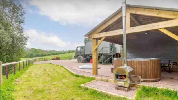 A covered outdoor area with a wooden structure, a barbecue grill, and a truck parked nearby. - Unique stay in your very own army truck. Sleeps 4. Hot tub. Tranquil setting. (Llangwm)
