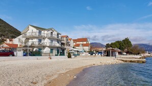 A coastal building with multiple balconies, a sandy beach, and clear water. - Apartments Rosić Baošići (Baošici)