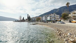 A lakeside promenade with buildings, a clear sky, and a mountain backdrop. - Apartments Rosić Baošići (Baošici)