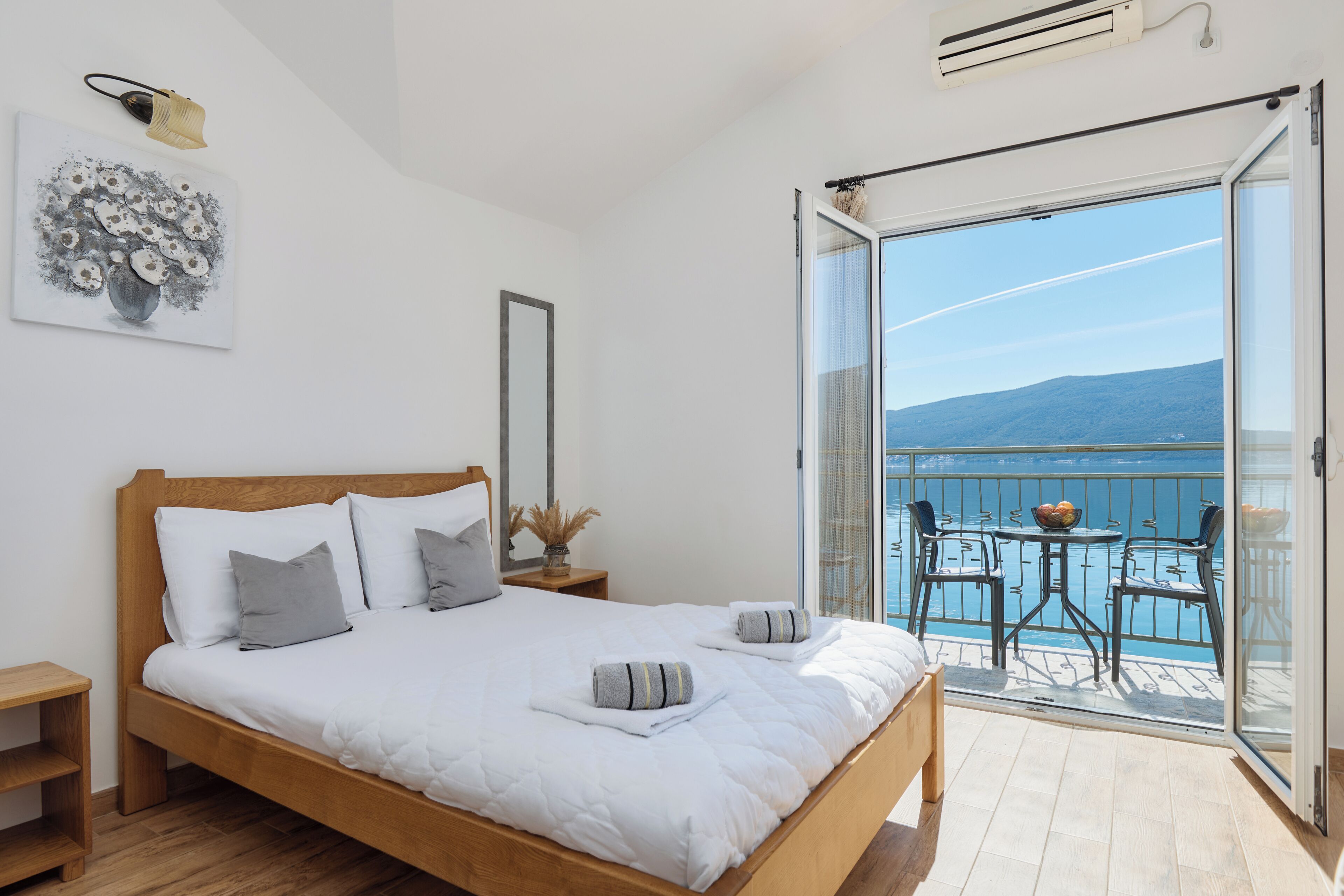 Un dormitorio con cama de madera, mesita de noche, un cuadro enmarco y balcón con vista al mar.